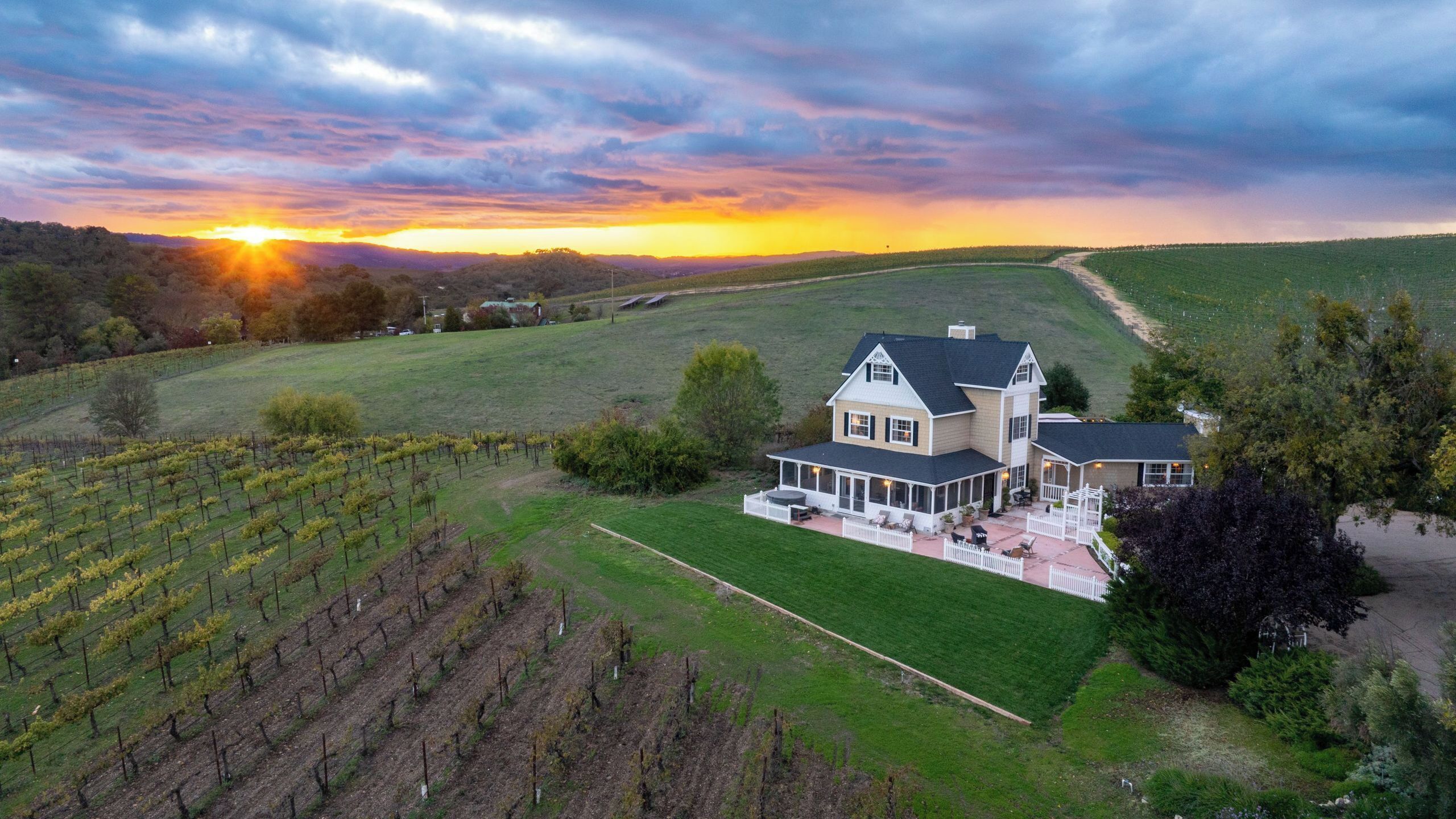 A large house with a spacious patio and a vineyard in the background.