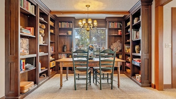 Una biblioteca con estanterías de madera, una mesa de comedor, sillas y una araña.