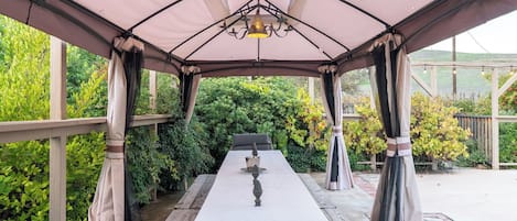 Une terrasse extérieure couverte, avec une table et des chaises, entourée de verdure.