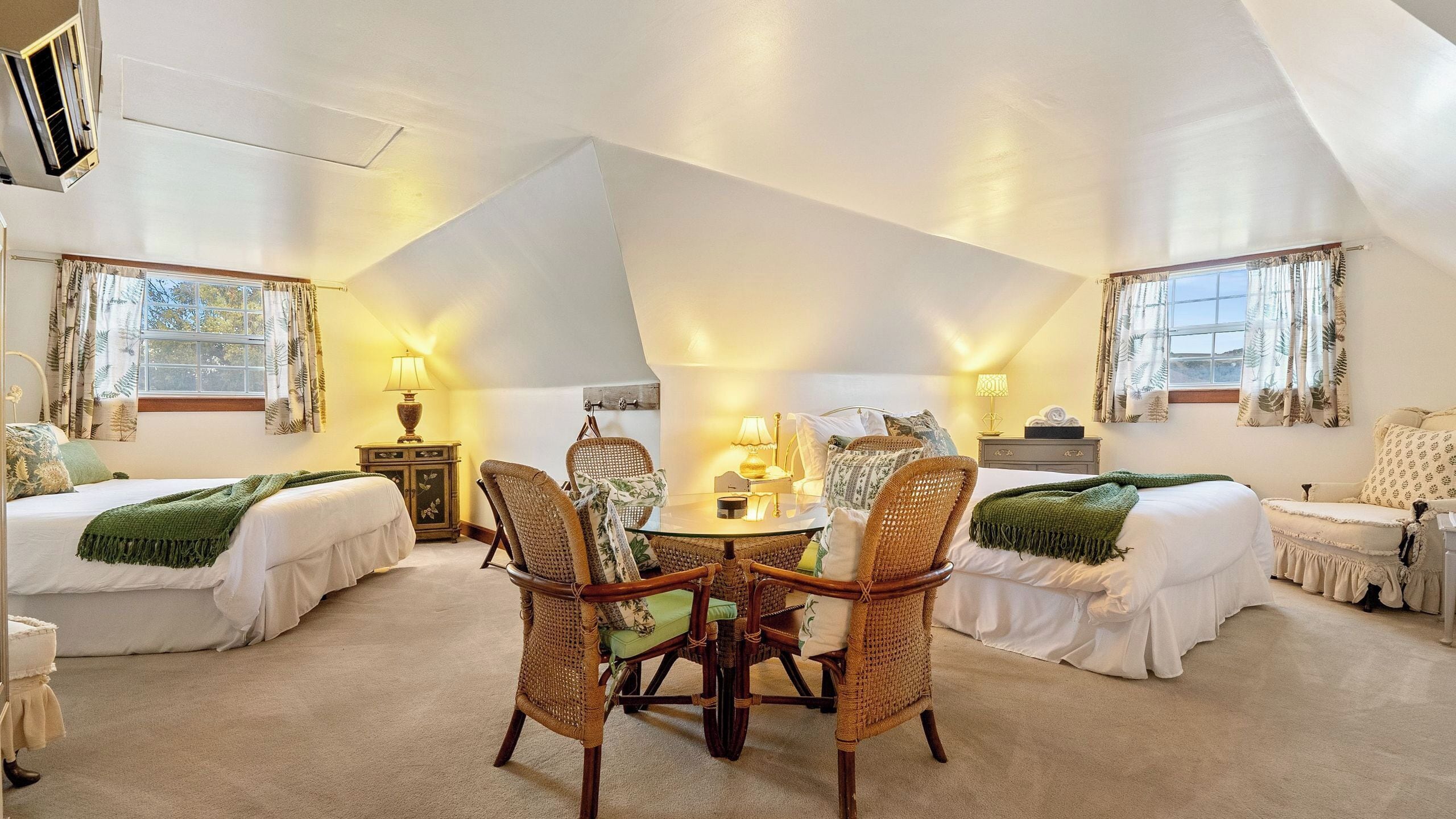 A spacious room with a high ceiling, two beds, a round dining table, and wicker chairs.