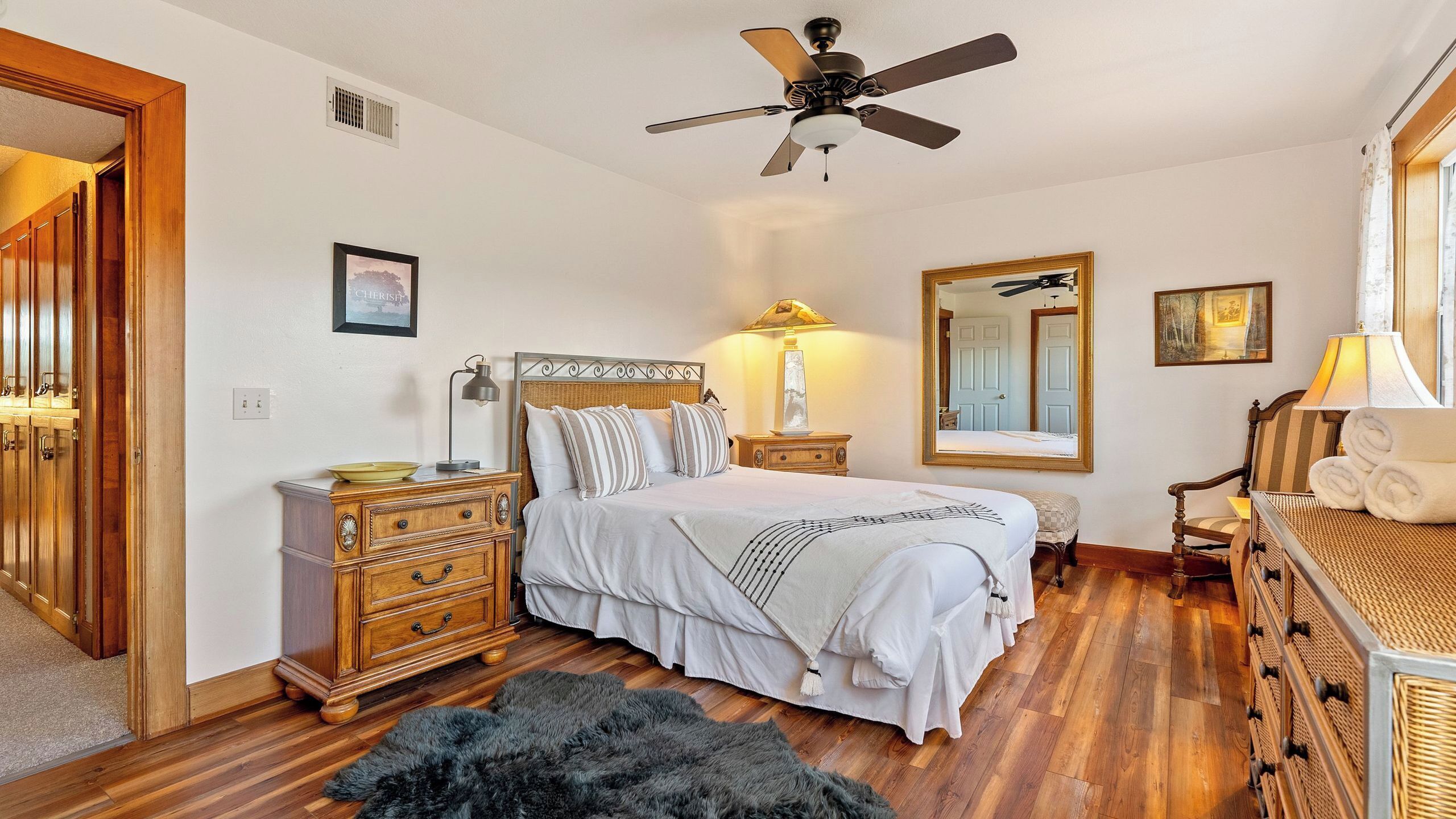 A bedroom with a bed, dresser, nightstand, lamp, mirror, and ceiling fan.