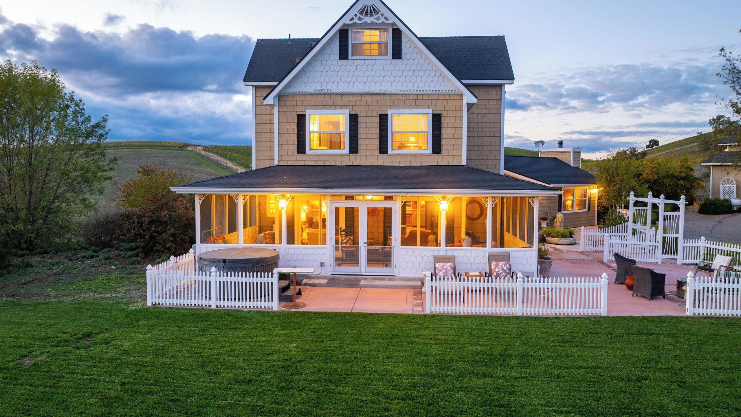 A two-story house with a covered patio area, a fenced yard, and a view of the surrounding landscape.