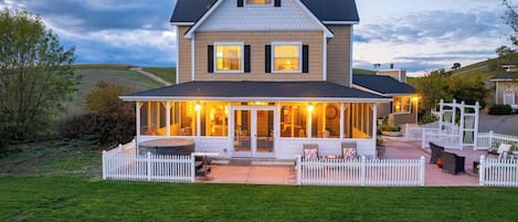A two-story house with a covered patio area, a fenced yard, and a view of the surrounding landscape.