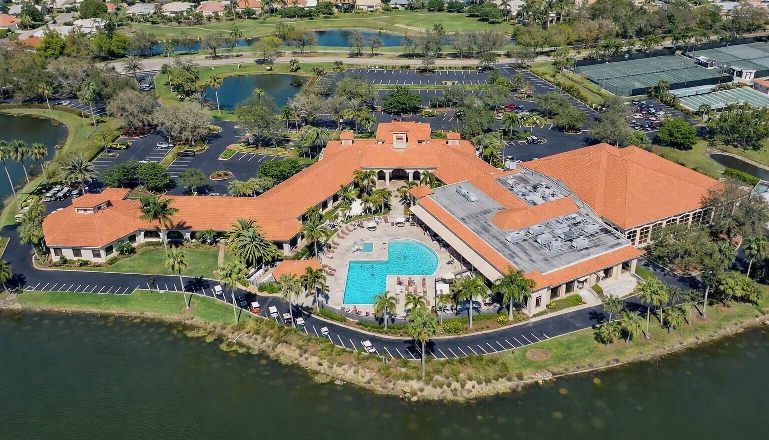 An aerial view of a resort with a swimming pool, parking areas, and a golf course.