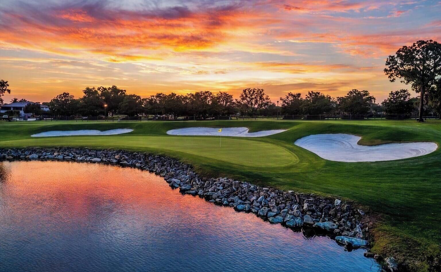 Un campo de golf con búnkeres, un obstáculo acuático y un cielo al atardecer.