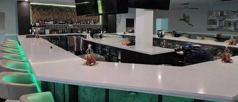 A bar area with a long counter, multiple seating options, and a variety of bottles and glasses.
