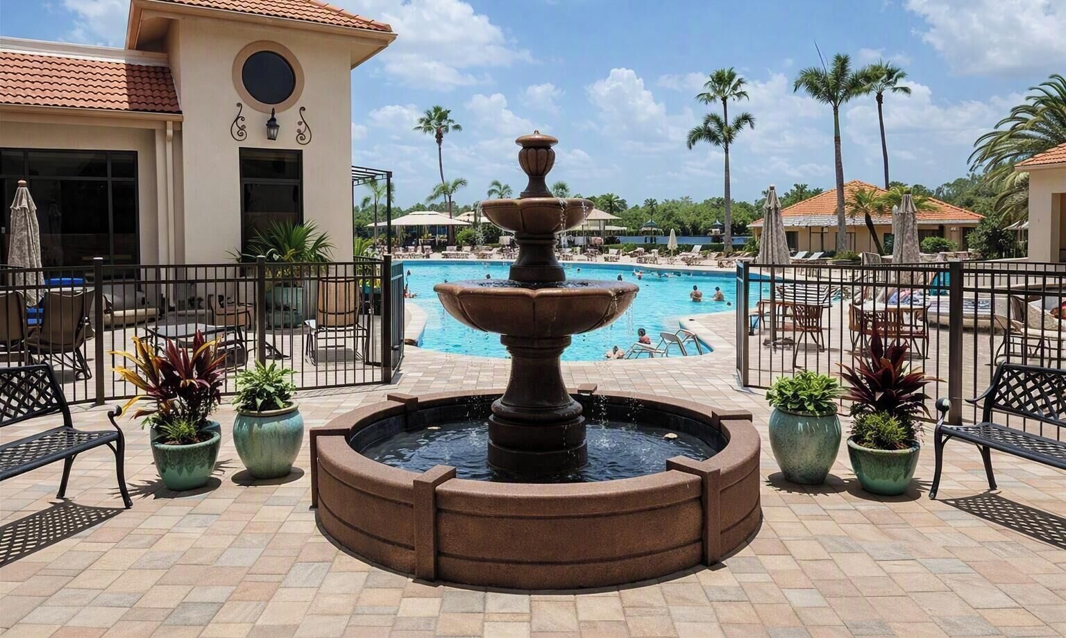 A pool area with a central fountain, surrounded by potted plants and outdoor seating.