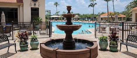 A pool area with a central fountain, surrounded by potted plants and outdoor seating.