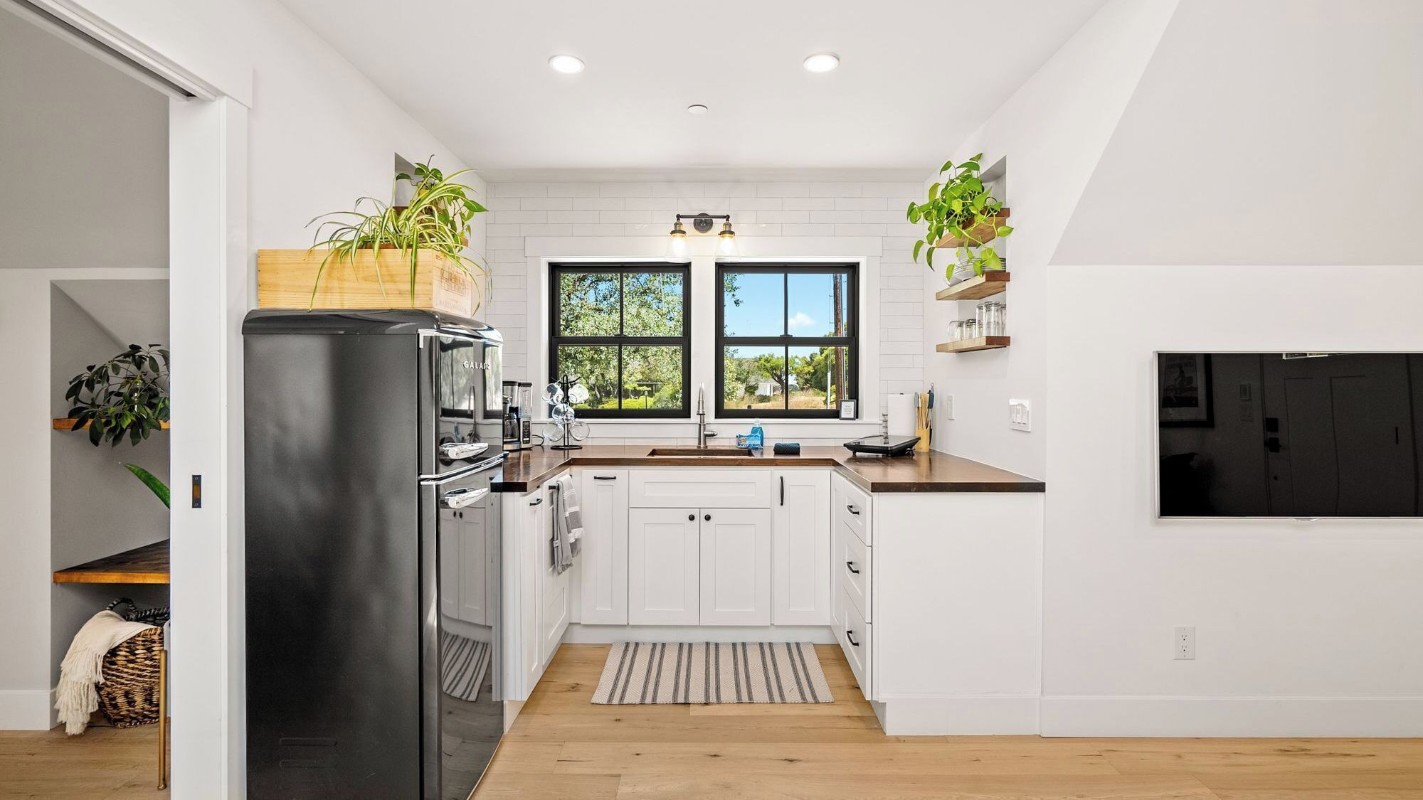 A modern kitchen with white cabinetry, a black refrigerator, and a window with a view of greenery.