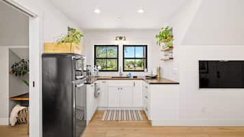 A modern kitchen with white cabinetry, a black refrigerator, and a window with a view of greenery.