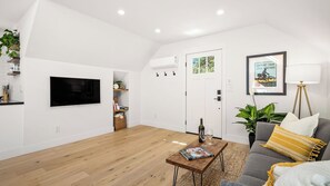 Ein modernes Wohnzimmer mit Flachbildfernseher, Couchtisch mit Zeitschrift, einer Couch mit Kissen und einer Stehlampe.