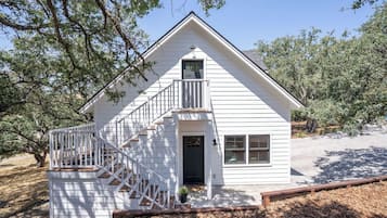 A white two-story house with a front porch, a staircase, and a small balcony.