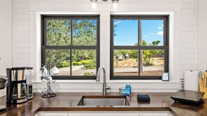 A kitchen with a large window, a coffee maker, a sink, and a countertop.