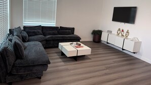 Een moderne woonkamer met een modulaire bank, een salontafel, een aan de muur bevestigde televisie en een plafondventilator.