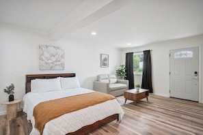 Un dormitorio con cama, una silla, una mesita y una puerta.