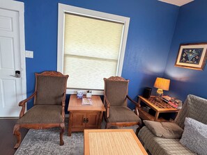 A room with two wooden chairs, a small table, a sofa, a window with blinds, a lamp, and a framed picture on the wall. - Prime location walk to BART: 2-bedroom house for your getaway, pet friendly (El Cerrito)
