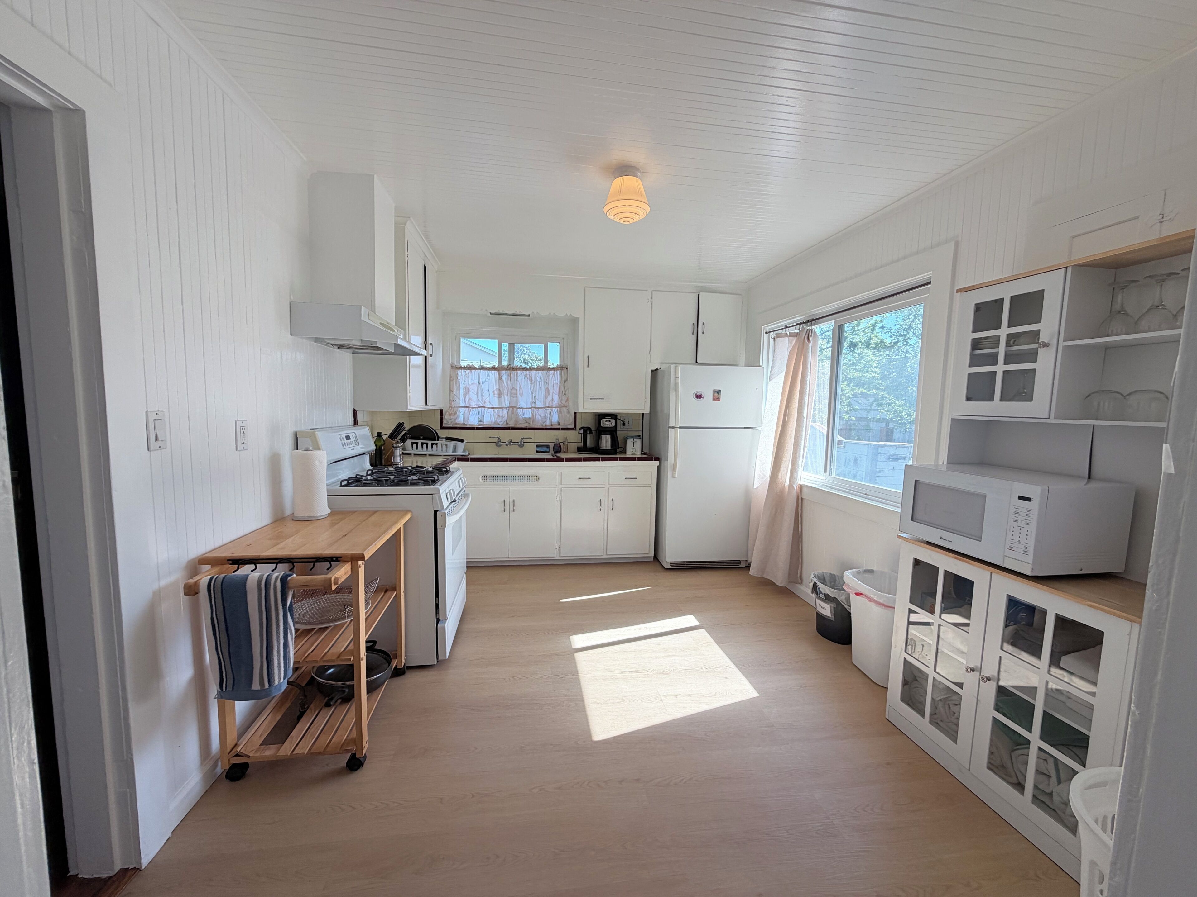 A compact kitchen with white cabinetry, a gas stove, a refrigerator, and a microwave.