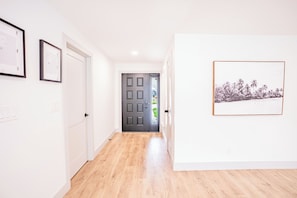 A hallway with a wooden floor, white walls, and a door leading to a room. There are framed pictures on the walls. - Modern Designer 3BD 2BA Pool Retreat 5 min to Beach (Seminole)