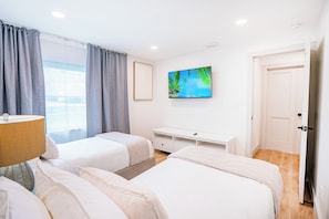 A hotel room with two beds, a TV on the wall, a desk, and a window with curtains. - Modern Designer 3BD 2BA Pool Retreat 5 min to Beach (Seminole)