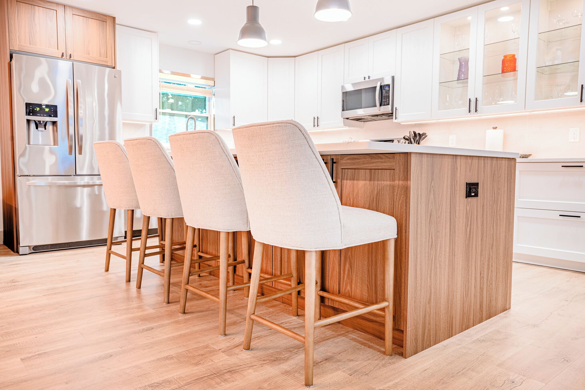A modern kitchen with a central island, bar stools, a stainless steel refrigerator, and white cabinetry.
