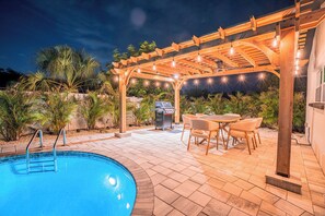 A swimming pool with a wooden pergola overhead, surrounded by patio furniture and palm trees. - Modern Designer 3BD 2BA Pool Retreat 5 min to Beach (Seminole)