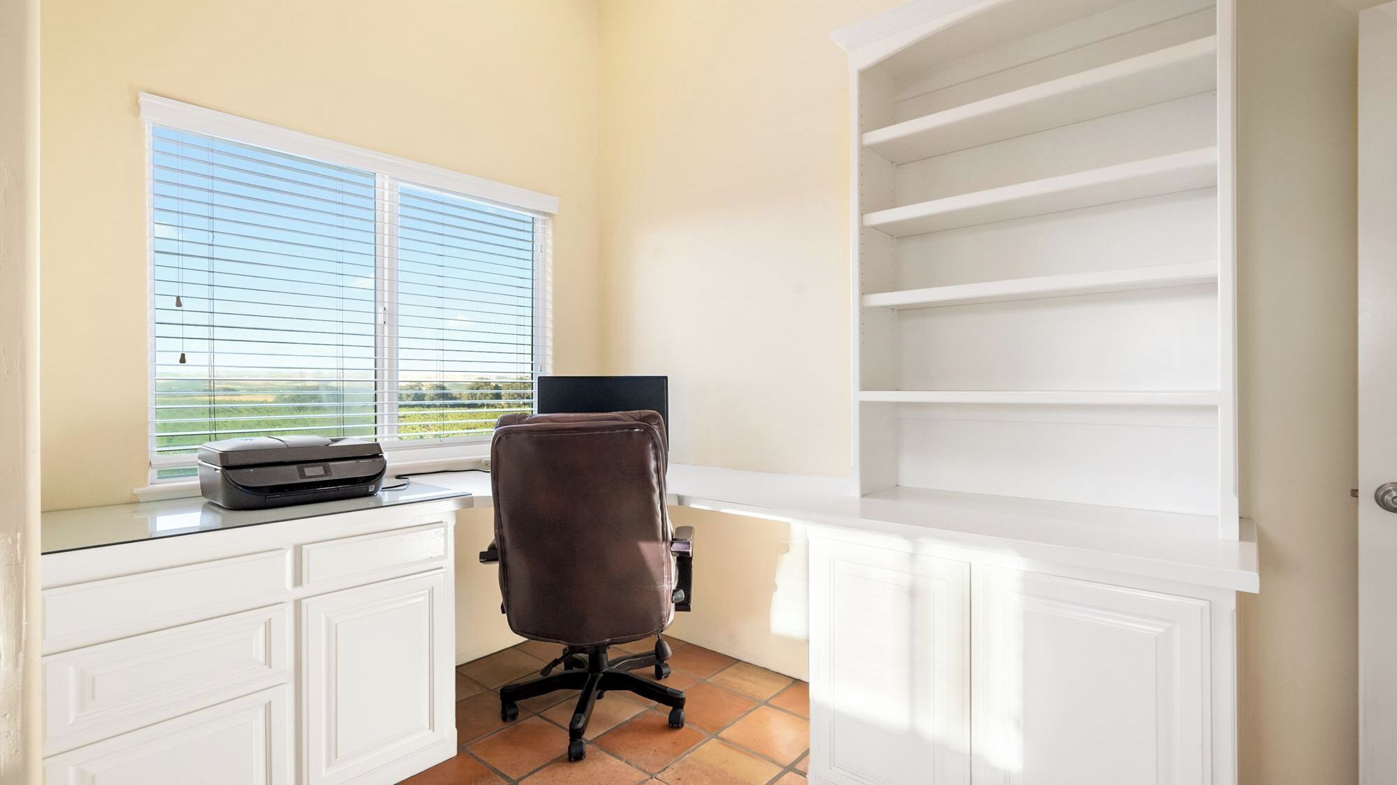 A home office with a desk, chair, printer, and a window with blinds.