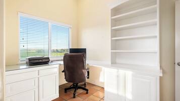 A home office with a desk, chair, printer, and a window with blinds.