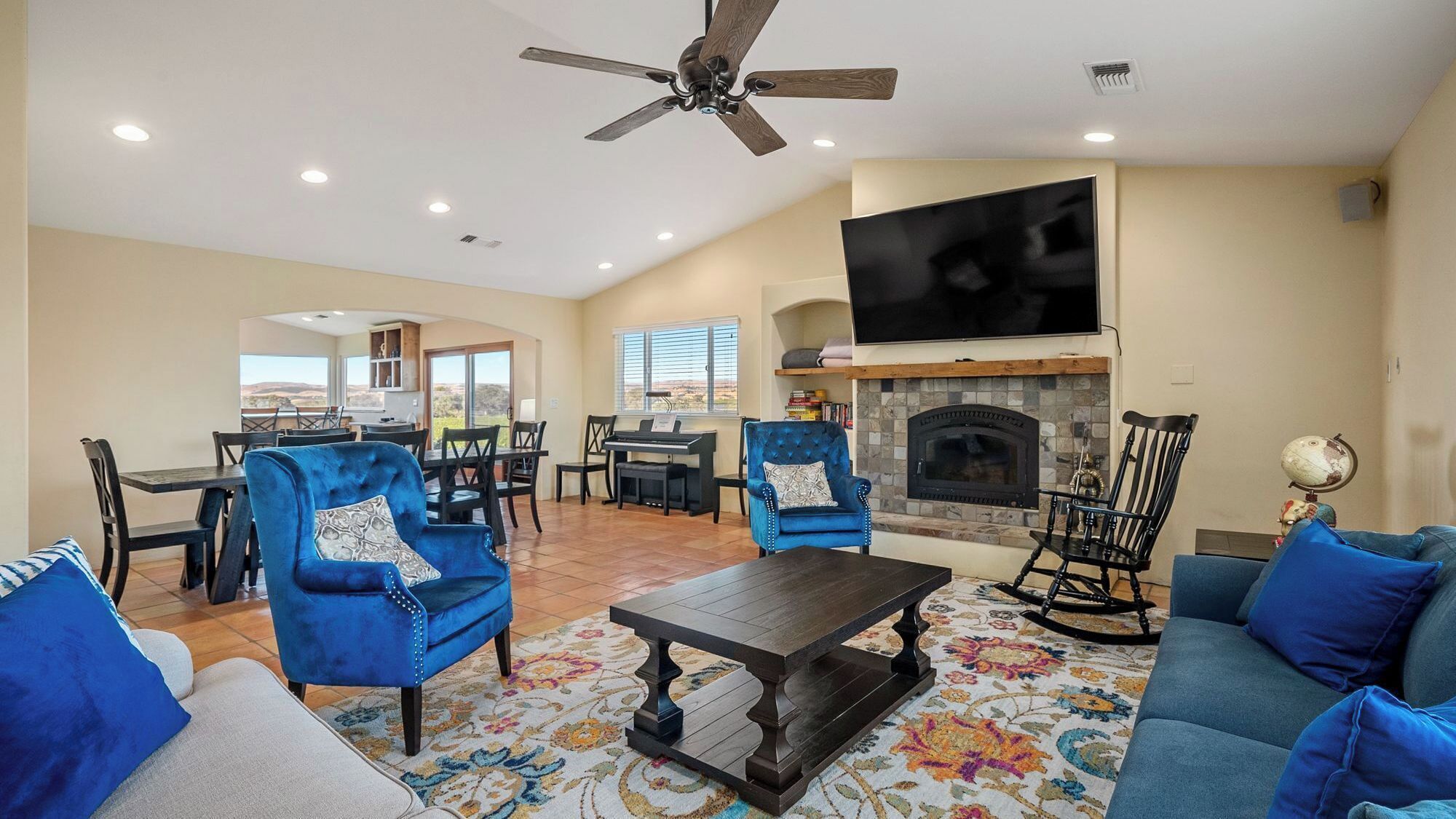 A spacious living room with a fireplace, a ceiling fan, and a large TV.