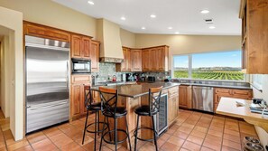 A kitchen with a large island, stainless steel appliances, wooden cabinets, and a view of a vineyard. - Wild Vines by Avantstay Vineyard Views + BBQ Patio Paso Robles Wine Country (Paso Robles)