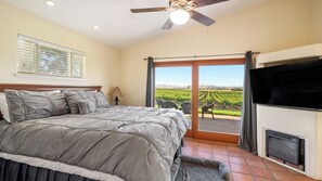 A bedroom with a bed, a ceiling fan, a TV, and a view of a vineyard through a sliding glass door. - Wild Vines by Avantstay Vineyard Views + BBQ Patio Paso Robles Wine Country (Paso Robles)