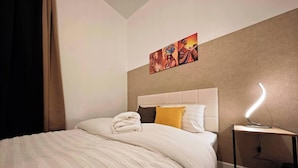 A hotel room with a bed, a nightstand, a lamp, and artwork on the wall.