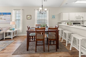 A dining area with a wooden table, four chairs, a chandelier, and a kitchen with white cabinets. - River Oaks 49I Myrtle Beach (Myrtle Beach)