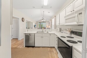 A modern kitchen with white cabinetry, a built-in dishwasher, a stove, and a microwave. - River Oaks 49I Myrtle Beach (Myrtle Beach)