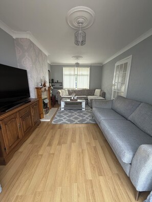 Un salon avec un téléviseur à écran plat, un canapé gris, une table basse et un tapis à motifs.