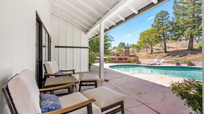 A covered patio with outdoor furniture, a swimming pool, and a view of a landscaped area.