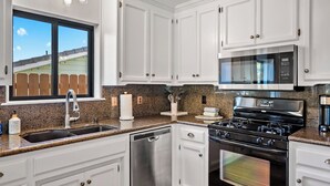 A kitchen with white cabinets, a stainless steel dishwasher, a black stove, and a microwave. - Prickly Pear Paso by Avantstay Fire Pit + BBQ Patio Walkable Downtown Paso (Paso Robles)