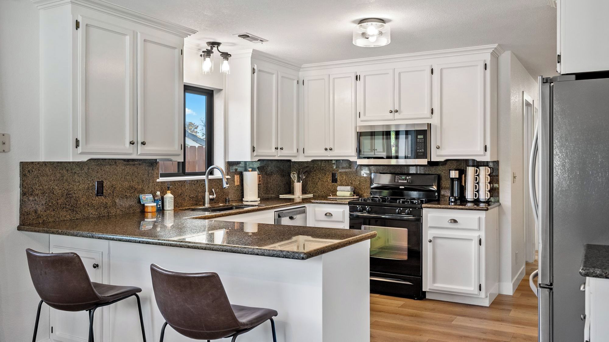 A modern kitchen with white cabinetry, granite countertops, a black stove, and stainless steel appliances.