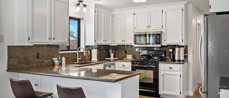A modern kitchen with white cabinetry, granite countertops, a black stove, and stainless steel appliances.