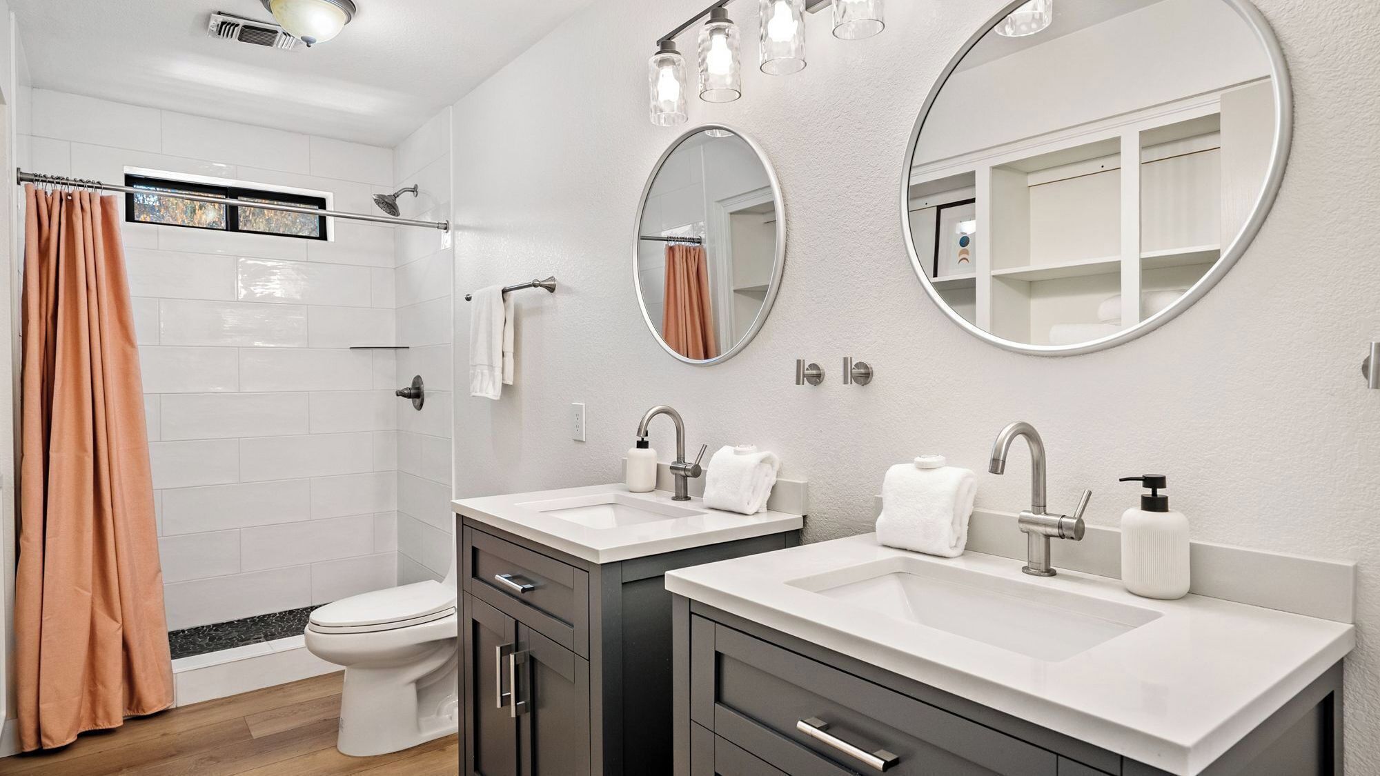 A modern bathroom with two sinks, a toilet, a shower, and a large mirror.