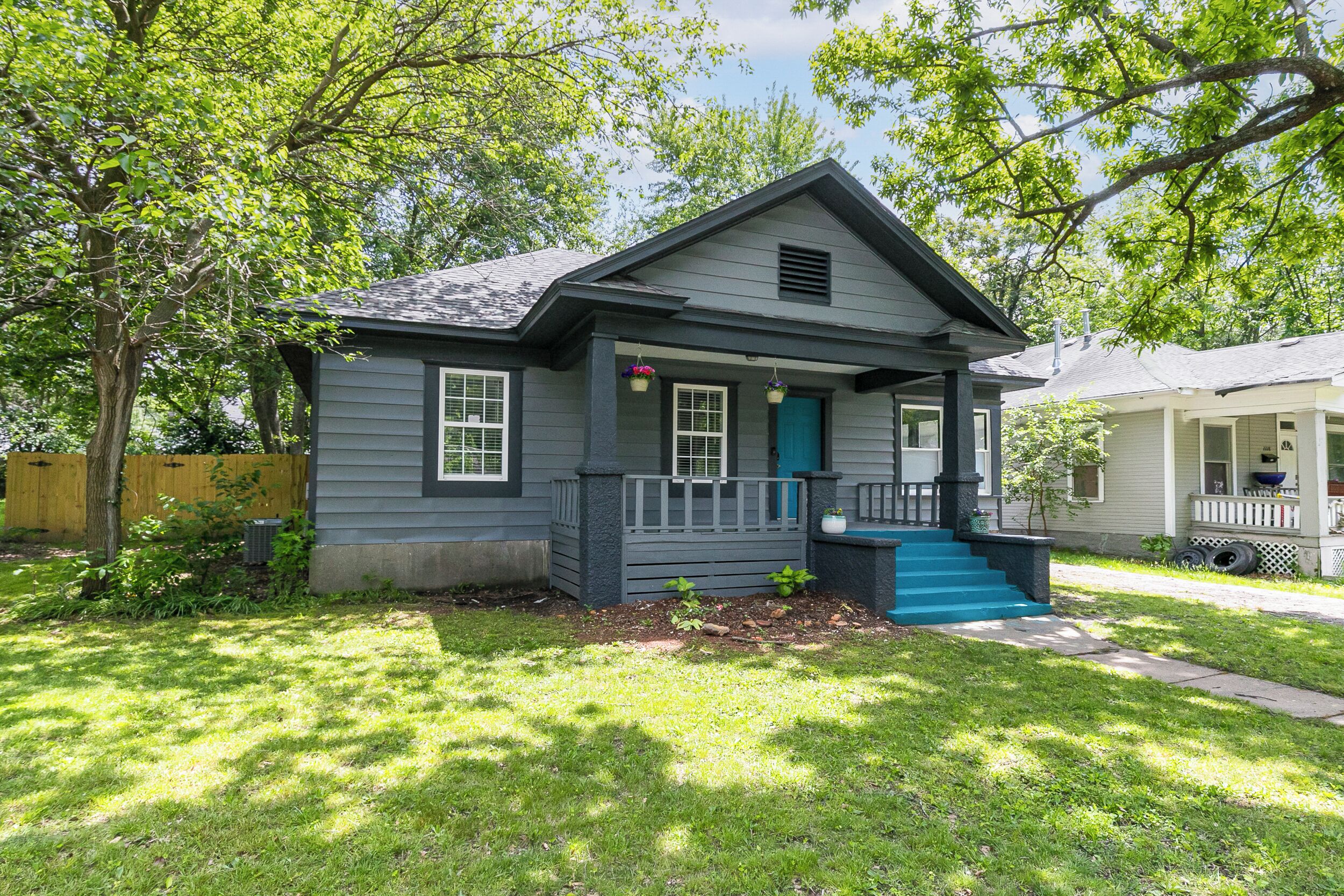 A small, single-story house with a front porch, a blue door, and a small set of stairs leading up to the entrance.