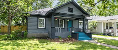 A small, single-story house with a front porch, a blue door, and a small set of stairs leading up to the entrance.