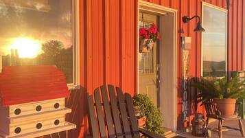 A red building with a wooden chair outside, a birdhouse, and a welcome sign.