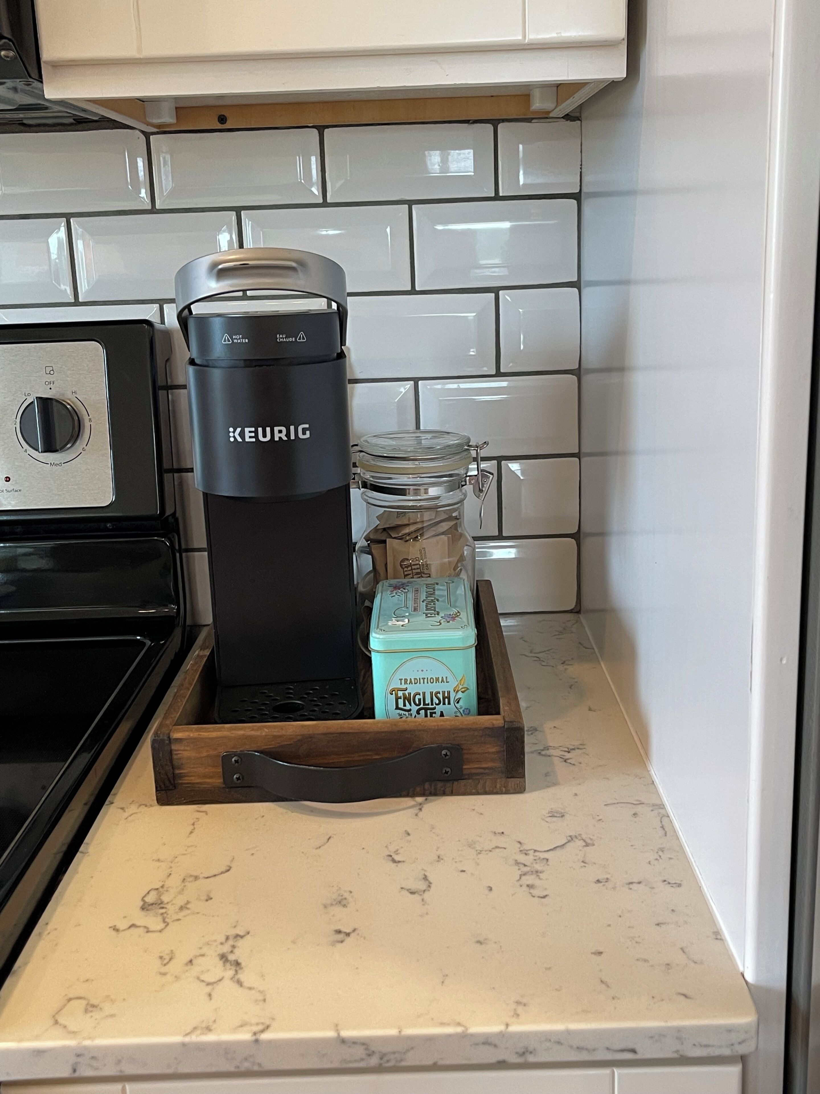 Una cocina con una cafetera Keurig, una bandeja de madera con una lata de té inglés y un microondas.