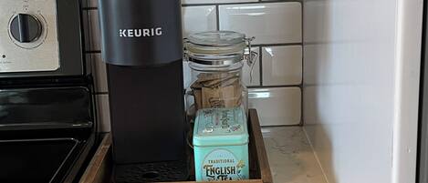 Una cocina con una cafetera Keurig, una bandeja de madera con una lata de té inglés y un microondas.