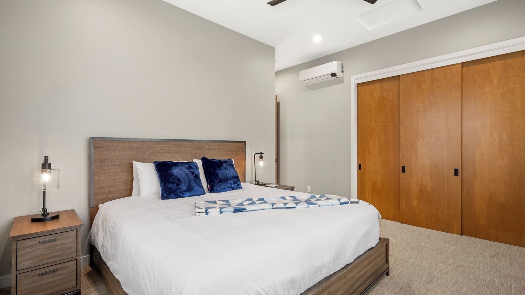 A hotel room with a bed, nightstands, an air conditioning unit, and a wardrobe.