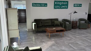 A modern living area with a sofa, a coffee table, and a lamp. There are street signs on the wall indicating 'Stockton Hill Rd' and 'Kingman City Limits.'