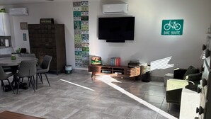 A modern living space with a dining area, a flat-screen TV mounted on the wall, and a sign indicating a bike route.