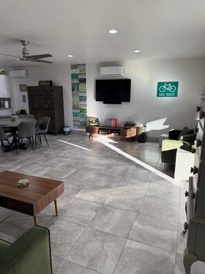 A modern living space with a dining area, a flat-screen TV mounted on the wall, and a sign indicating a bike route.