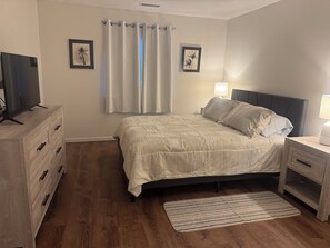 Une chambre à coucher avec un lit, une table de chevet avec une lampe, une commode et un téléviseur posé sur un meuble.