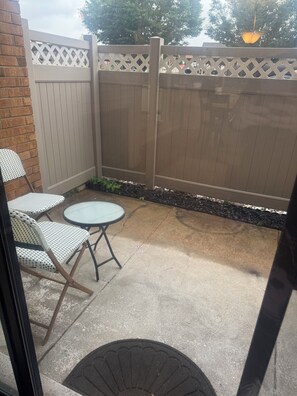 Un espace patio agrémenté d’une clôture blanche, d’une table ronde et de deux chaises en osier.